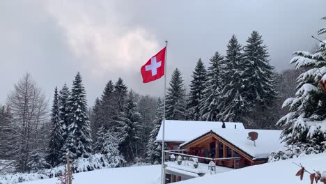 switzerland flag flying over the swiss alps in the winter with a traditional chalet