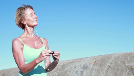 mujer de edad avanzada en forma haciendo una pausa en su carrera para cambiar su música