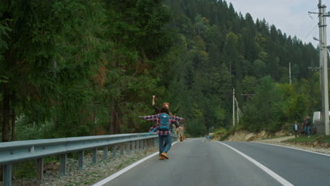 Happy-hikers-trekking-roadside-in-mountains-landscape.-Two-friends-raising-hands