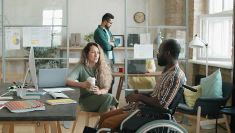 african american man with disability talking with female colleague over coffee in office