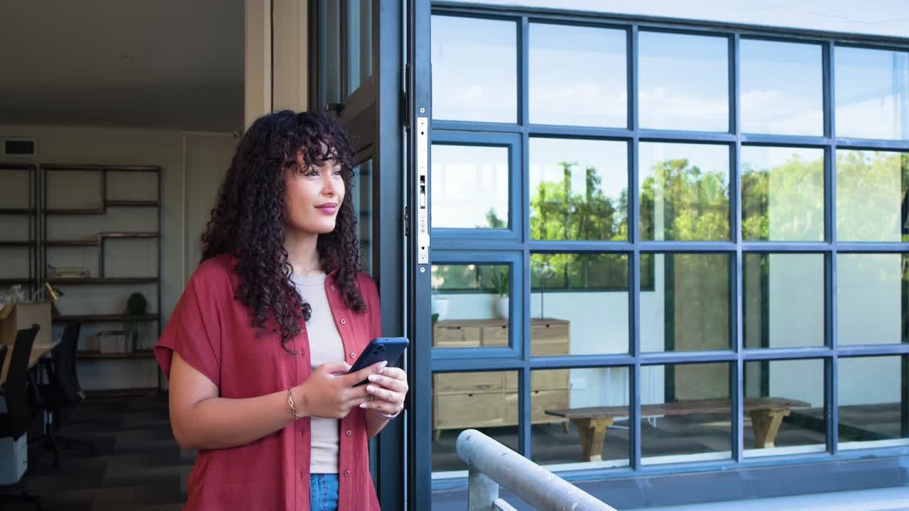 Woman holding smartphone, reading message, smiling and laughing, leaning at office door, copy space