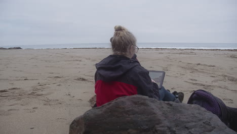 Frau-Sitzt-Allein-Zeichnung-Auf-Tablette-Im-Freien-Bei-Rinsy-Head-And-Cove-In-Cornwall,-England,-Vereinigtes-Königreich