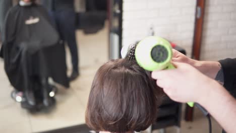 un peluquero profesional está secando el cabello de una mujer joven y atractiva en un salón de belleza. filmado en 4k