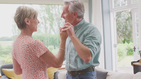 Romantic-Senior-Retired-Couple-Dancing-In-Lounge-At-Home-Together