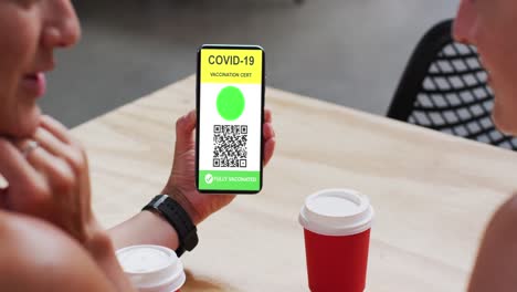 hombre en un café mostrando un teléfono inteligente con certificado de vacunación contra la covid y código qr en la pantalla