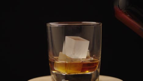 drink being poured in a glass with ice cubes in it