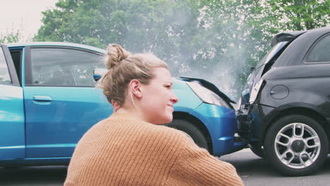 mujer automovilista con la cabeza en las manos sentada al lado de los vehículos involucrados en un accidente automovilístico