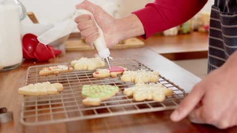 biracial man decorating christmas cookies in kitchen at home, slow motion