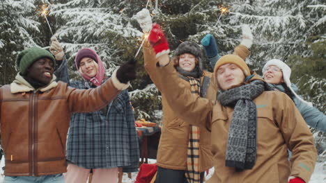 friends dancing with christmas sparklers in winter forest