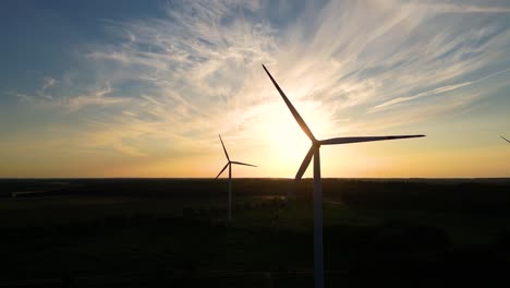 Große-Windkraftanlagen-Mit-Rotorblättern-Im-Feld,-Luftaufnahme,-Leuchtend-Orangefarbener-Sonnenuntergang,-Blauer-Himmel,-Windpark,-Zeitlupe,-Drohnendrehung