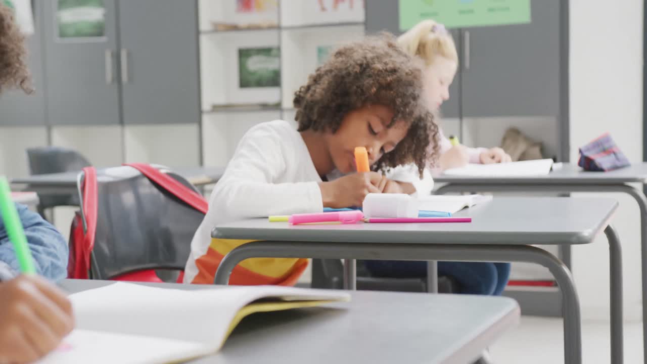 Video of diverse schoolchildren sitting at desks working during lesson