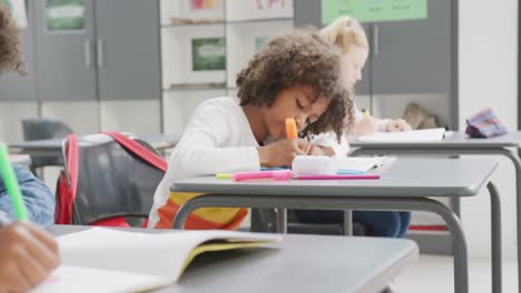 video of diverse schoolchildren sitting at desks working during lesson