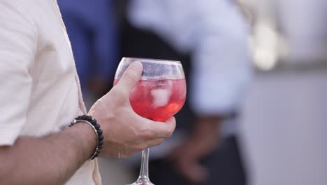 close up of a man's hand holding a glass of red cocktail with ice, creating a casual and festive vibe