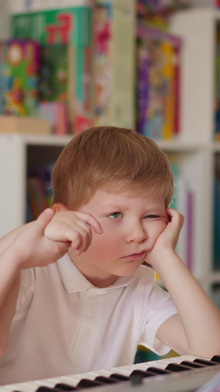 Little girl with french plaits forces disinterested junior brother to play piano holding fingers in children room. Sister tries to teach toddler boy musical composition