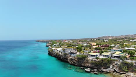 Pueblo-Costero-De-Curacao-Con-Mar-Turquesa-Y-Cielos-Despejados,-Vista-Aérea