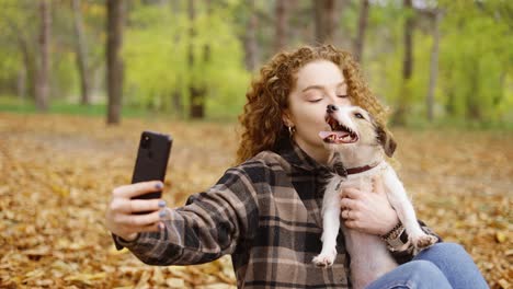 smiling young woman with dog outdoors in autumn making selfie