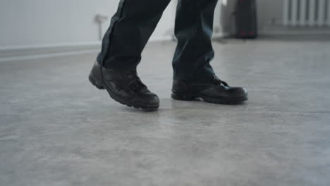 low angle view of person in black shoes and trousers turning away from chair with box on floor visible in background as one leg lifts mid-step on smooth polished surface in quiet indoor space