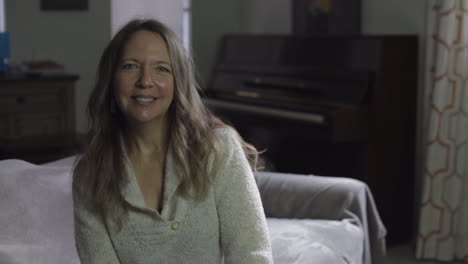 mature woman in her 30s or 40s smiling at the camera while sitting on a sofa