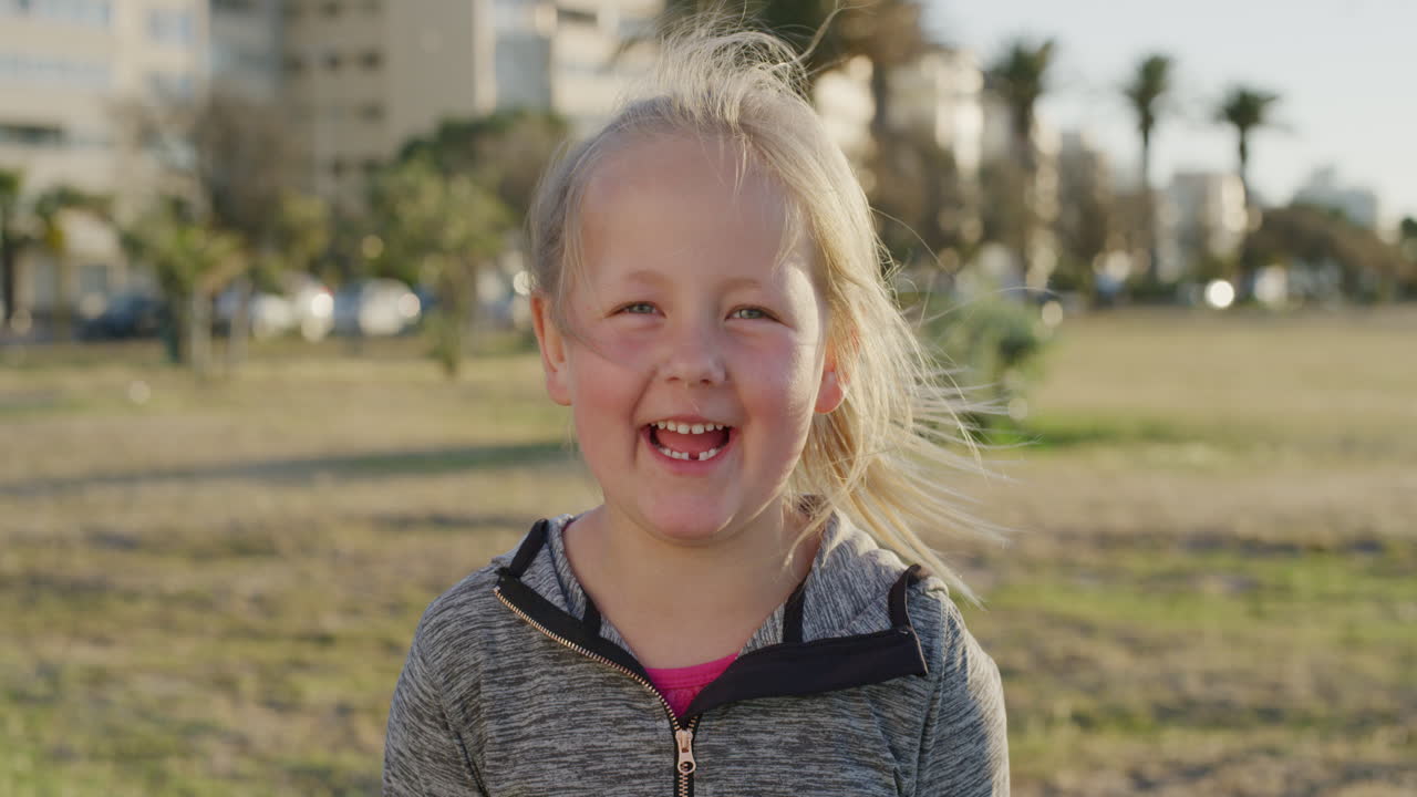 retrato de uma linda menina loira sorrindo feliz desfrutando de um dia de verão relaxado em um parque urbano ao pôr do sol em câmera lenta