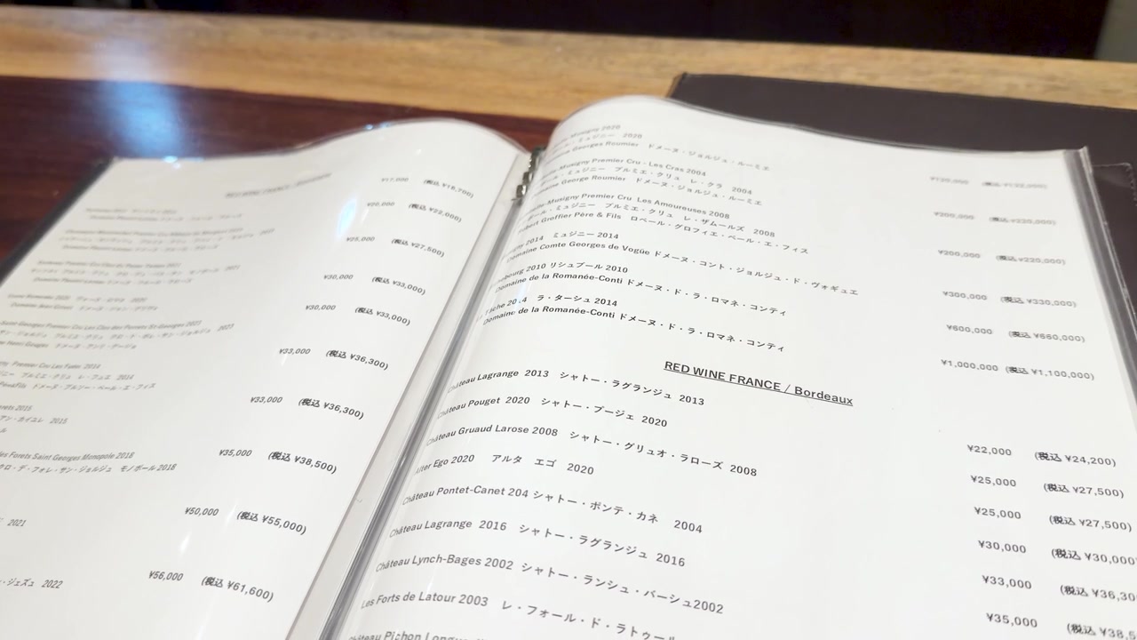 A person flips through a detailed wine menu inside a dimly lit Japanese restaurant interior
