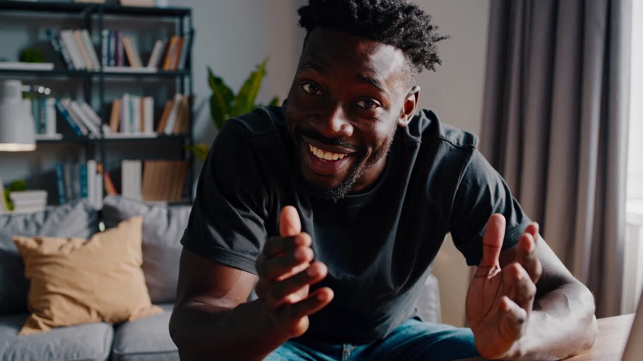 Casual video call setup with a man smiling at a laptop. Shot from a low angle, showcasing a cozy