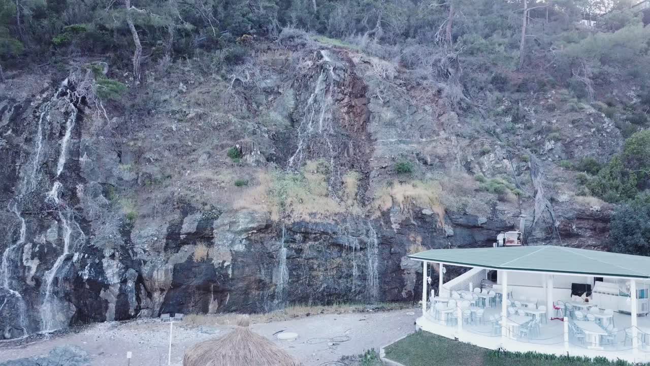 해변 에 있는 식당 근처 에 있는 바위 가 있는 절벽 을 따라 폭포 가 떨어지고 있다