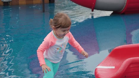 adorable blonde three years old girl with pigtails sliding down at water slide at outdoor aquapark playground and running fast for next turn