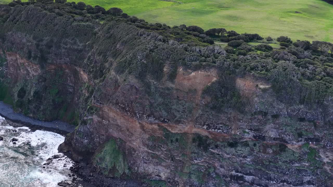 Drone glides above rugged cliffs and ocean waves, natural daylight, wide sweeping landscape perspective