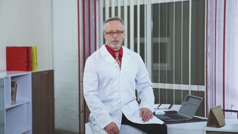 physician recording webinar training. professional male doctor sitting on desk and talking in healthcare center. doctor in glasses and white medical uniform looking at camera.