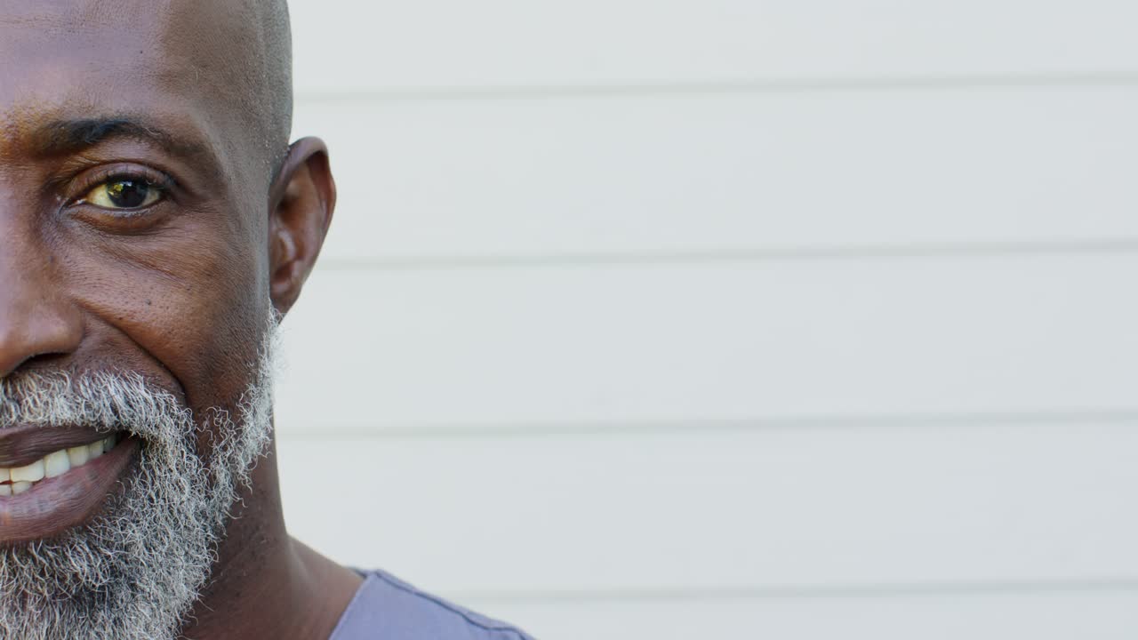 Senior African American man holding neutral, smiling warmly in scrub top on pale siding, copy space