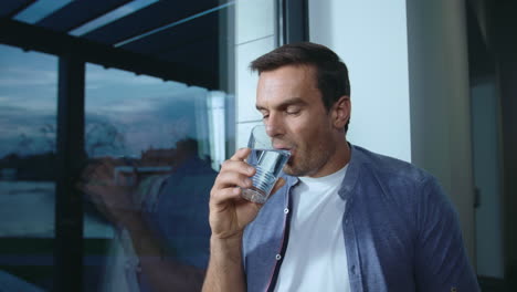 Relaxed-business-man-drinking-water-near-panoramic-window