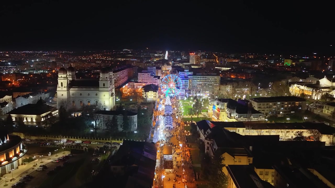 Veduta aerea notturna con drone del viale Stefan cel Mare, Iasi, Romania, con ruota panoramica illuminata e municipio della città