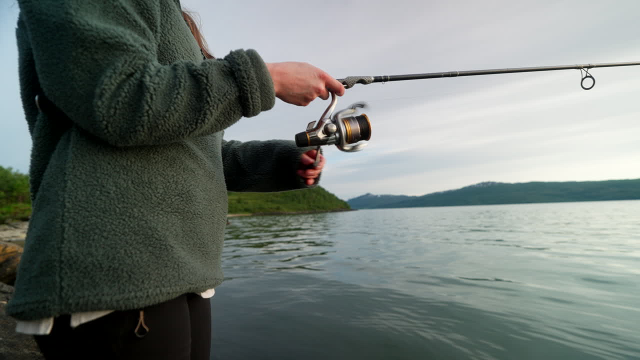Closeup side view of female fisherman reeling in during spin fishing in Norway