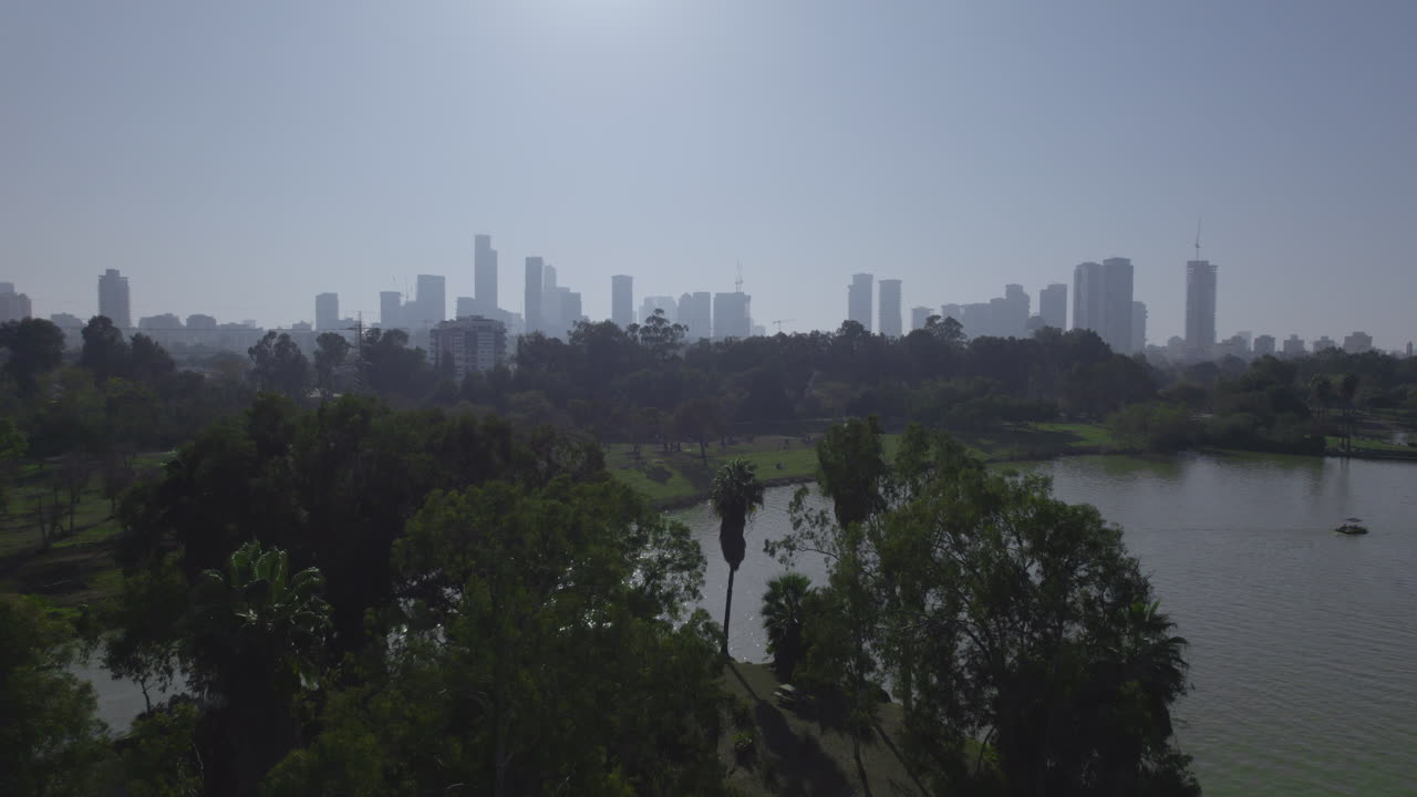 야르콘 공원의 나무 뒤에 있는 텔 아비브 타워를 드러내는 텔 아비브의 중심부에 있는 거대한 녹지, 피크닉, 자전거 대여, 보트 대여, 워터 파크 및 놀이터