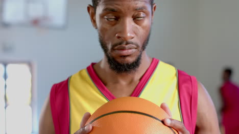 hombre afroamericano enfocado sosteniendo una pelota de baloncesto en un gimnasio