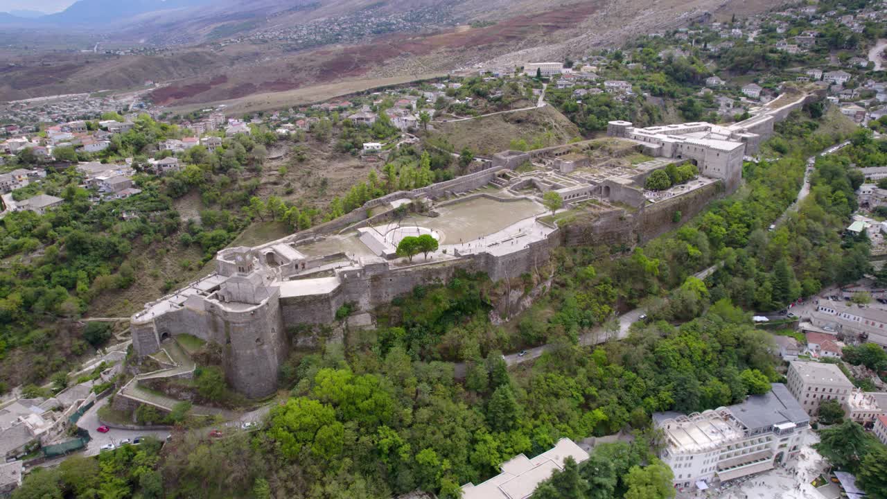 Ripresa aerea con drone di una grande fortezza storica in pietra su una collina circondata da alberi e una città vicina in un paesaggio montuoso, movimento fluido di panoramica della camera