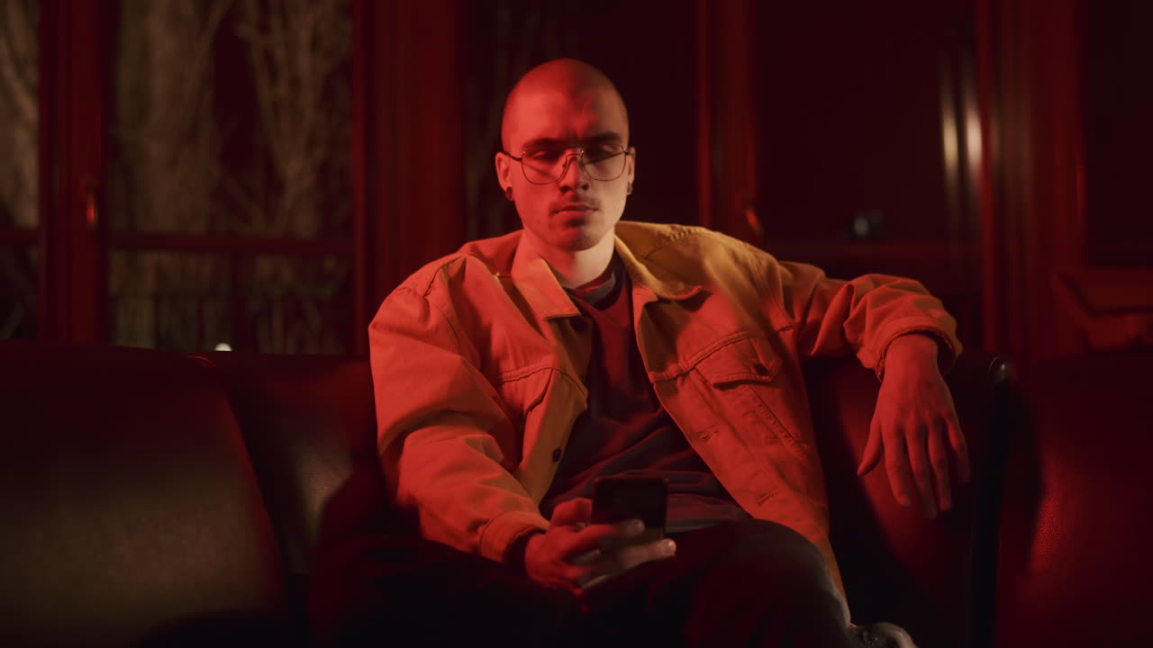 Man Sitting on Sofa with Smartphone in Red Light