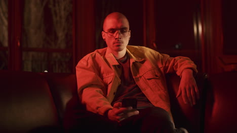 man sitting on sofa with smartphone in red light