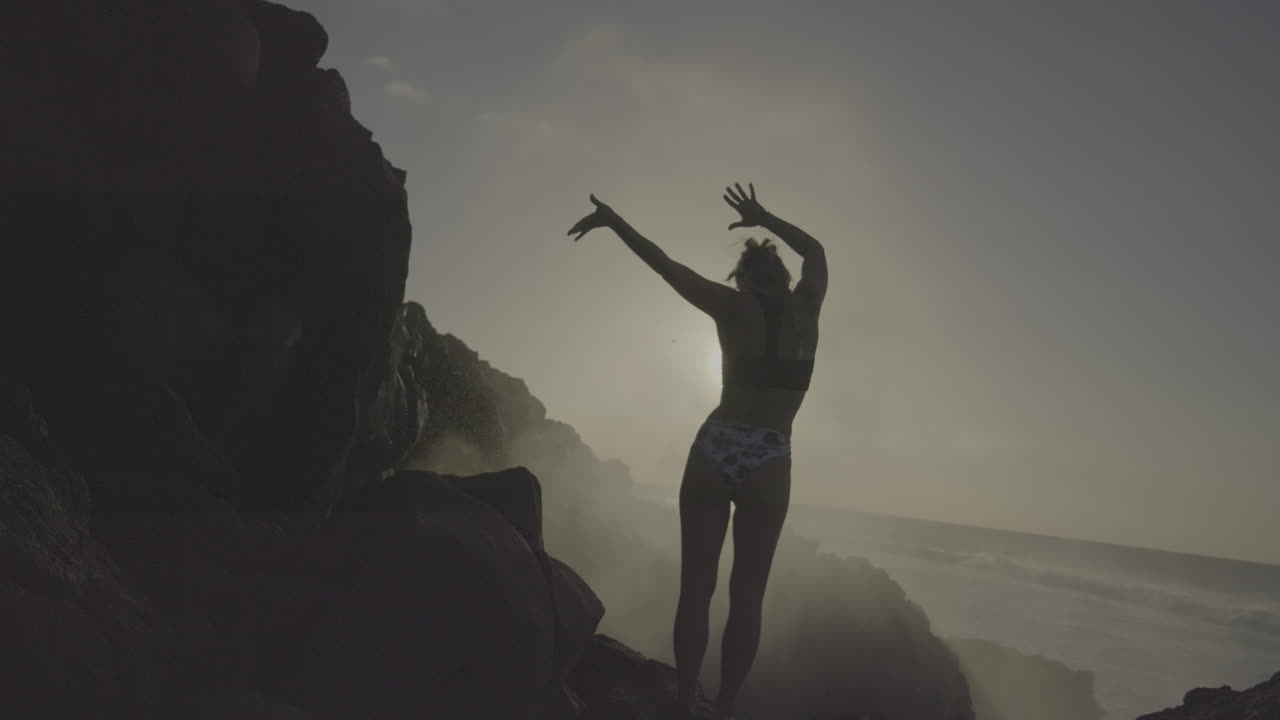 Woman enjoying a sunset view over the ocean from volcanic rocks
