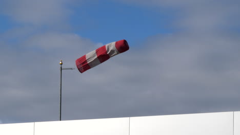 an isolated windsock at an airfield in heavy winds to a backdrop of white clouds and blue sky cropped