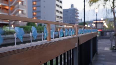 a shot capturing the cityscape of tokyo mizumachi along the kita-jūkken-gawa river at dusk. blue pinwheels line the promenade railing, and a sightseeing boat floats in the canal