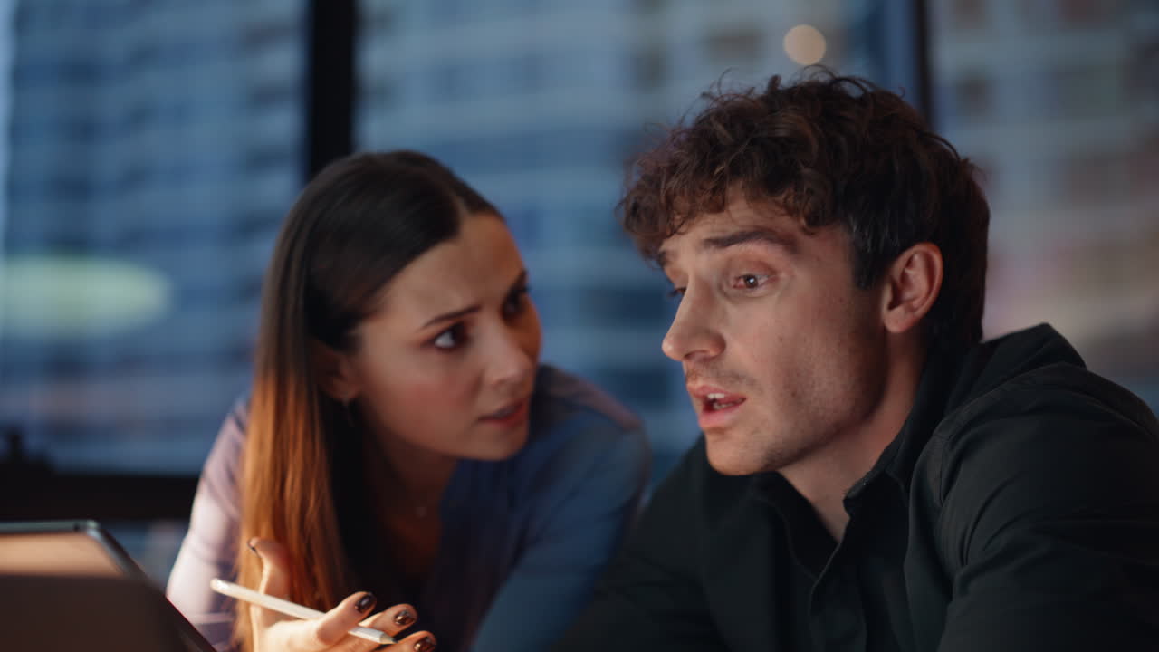 Two managers analyzing data on tablet discussing problems at dark office closeup