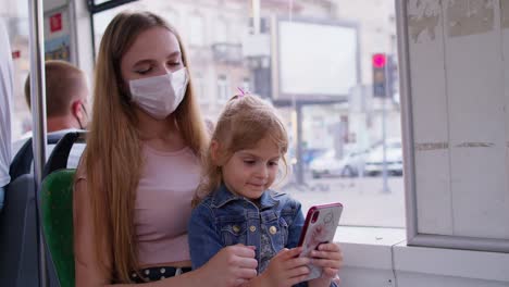 Tired-sleepy-woman-with-daughter-going-home-by-bus-after-hard-work-day,-child-kid-play-on-smartphone