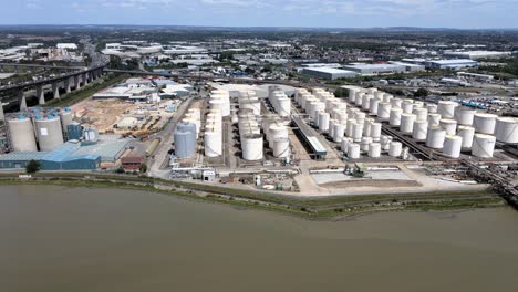 Industrial-Silos-at-Factory-Facility-by-River,-Aerial-Establishing