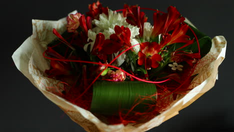 zoomed out a large bouquet of red and white flowers and green decorative elements in a glass vase decorated with paper around on a dark background