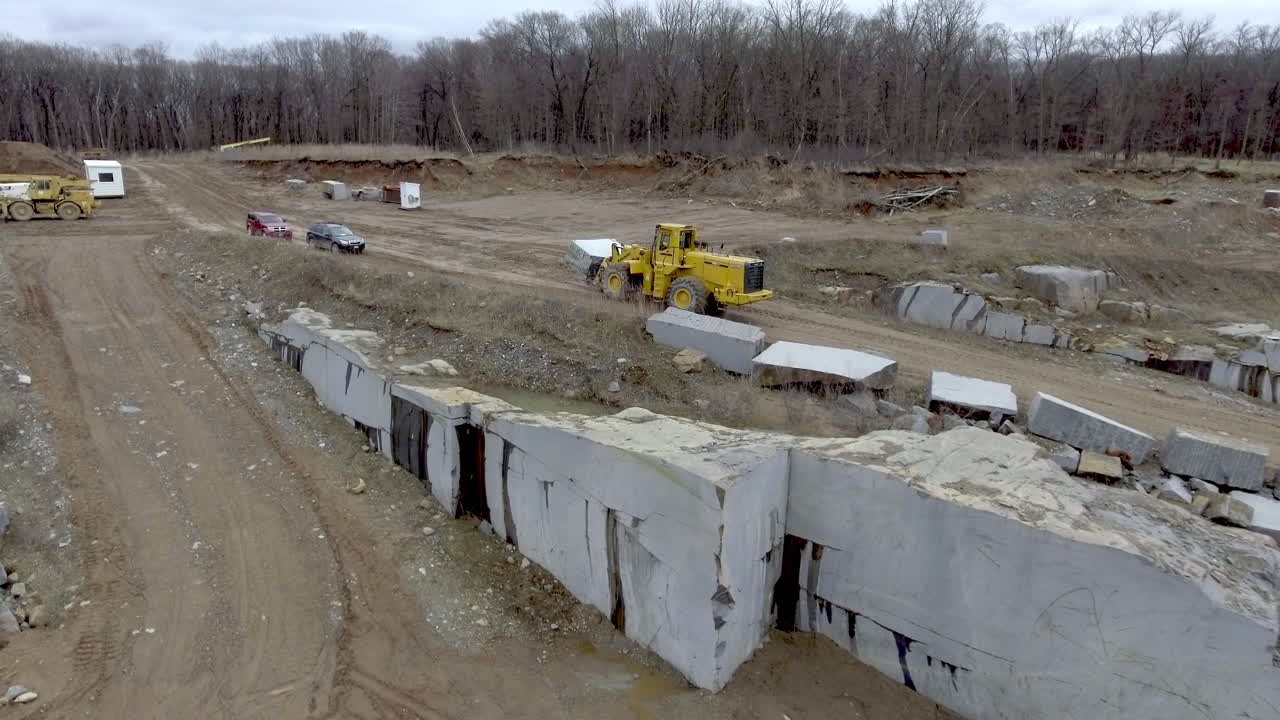cargador frontal de construcción que mueve un gran trozo de granito en un camino de tierra