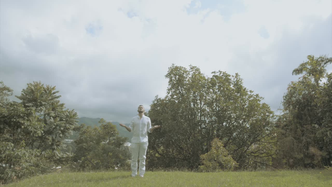 Young man in white Dress doing yoga meditation and spiritual movements in a beautiful green landscape mindfulness and tai chi
