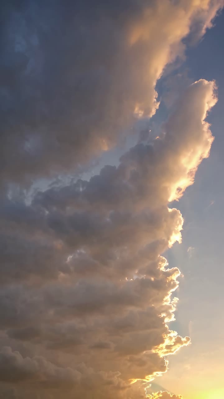 Dramatic upward angle of towering clouds at sunset, capturing golden hues and shadows
