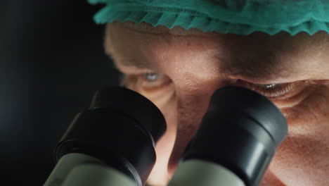 the face of a male researcher looking into the eyepiece of a microscope