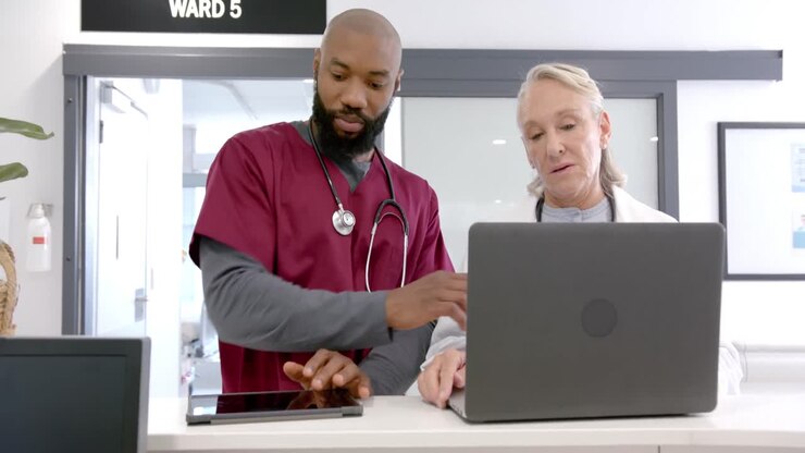 Diversi medici, uomini e donne, in discussione che usano un tablet e un laptop in ospedale, al rallentatore.